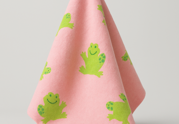 A pink baby blanket with little green frogs as a pattern.